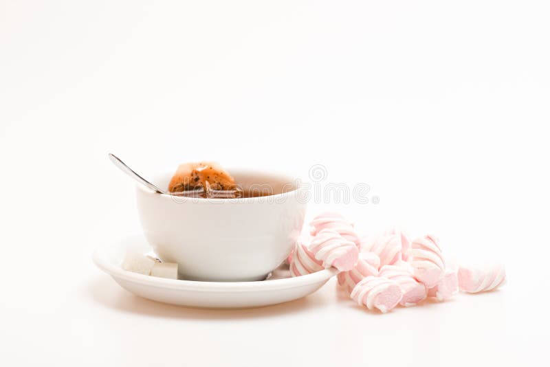 Tea mug with dipped teabag and marshmallows. Tea break concept. Process of drink brewing in cup. Mug filled with black brewed tea, spoon and heap of marshmallow on white background. Tea mug with dipped teabag and marshmallows. Tea break concept. Process of drink brewing in cup. Mug filled with black brewed tea, spoon and heap of marshmallow on white background.