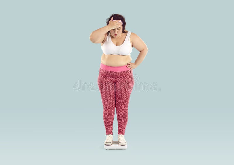 Overweight woman weighs herself. Big fat chubby plump obese lady isolated over light blue background stands on scales, looks at number, sees how many kilos she has gained and makes whistle of surprise. Overweight woman weighs herself. Big fat chubby plump obese lady isolated over light blue background stands on scales, looks at number, sees how many kilos she has gained and makes whistle of surprise