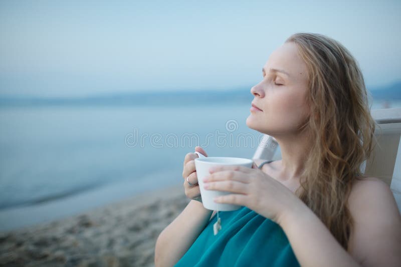 Woman with closed eyes enjoying a cup of tea at the seaside sitting relaxing on a deckchair with a blissful expression overlooking a tropical beach. Woman with closed eyes enjoying a cup of tea at the seaside sitting relaxing on a deckchair with a blissful expression overlooking a tropical beach