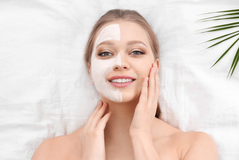 拥有粘土面膜和热带叶子的美丽女人，置于白色面料上 免版税库存图片