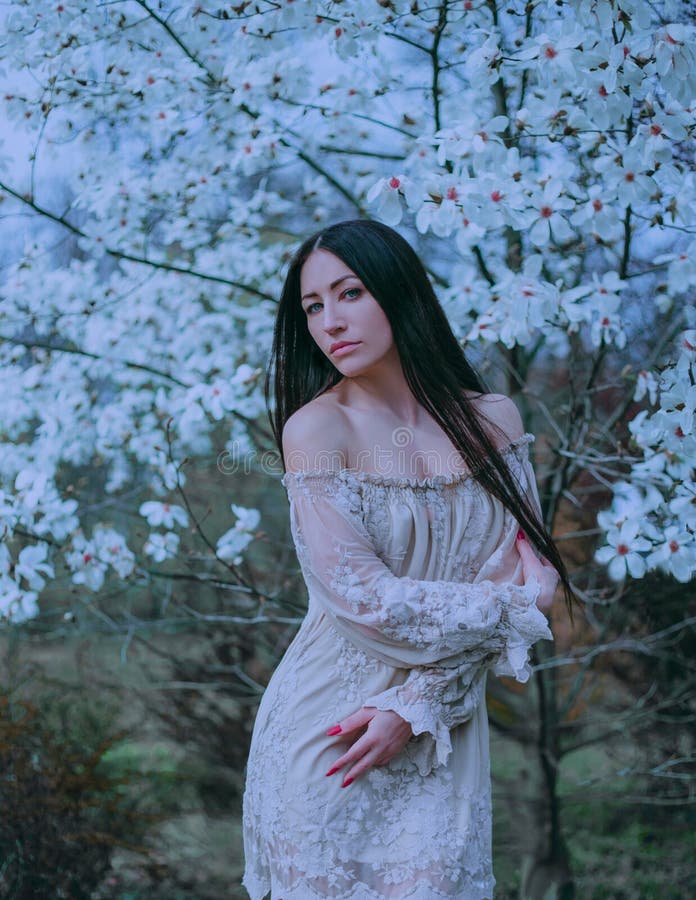 有黑暗的长发和嫉妒的逗人喜爱的可爱的夫人,站立在开花的木兰附近,穿戴令人愉快的葡萄酒 图库摄影 有黑暗的长发和嫉妒的逗人喜爱的可爱的夫人,站立在开花的木兰附近,穿戴令人愉快的葡萄酒 图库摄影