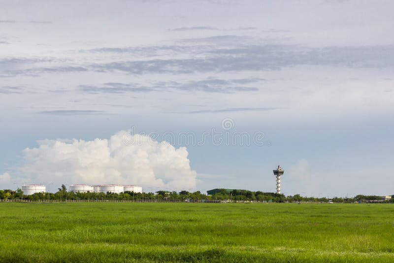机场空中交通管理的塔台与在油箱附近的绿色领域在多云天空背景在晚上 库存照片 机场空中交通管理的塔台与在油箱附近的绿色领域在多云天空背景在晚上 库存照片