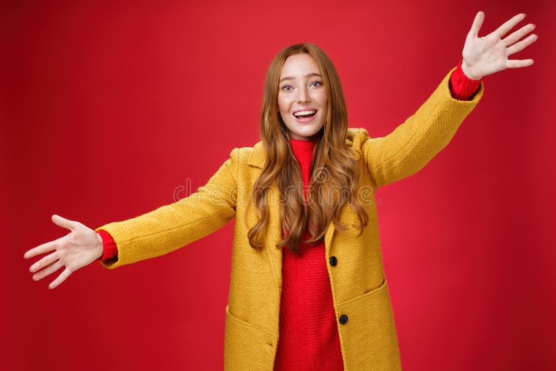 Hey come and hug me friend. Charming playful and emotional redhead female extanding palms forward to cuddle and greet, giving warm welcome smiling broadly posing in yellow coat over red wall. Hey come and hug me friend. Charming playful and emotional redhead female extanding palms forward to cuddle and greet, giving warm welcome smiling broadly posing in yellow coat over red wall.