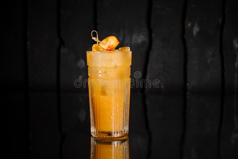 Glass of fresh alcoholic drink with ice decorated with pieces of peach served on the dark surface. Drink concept. Glass of fresh alcoholic drink with ice decorated with pieces of peach served on the dark surface. Drink concept