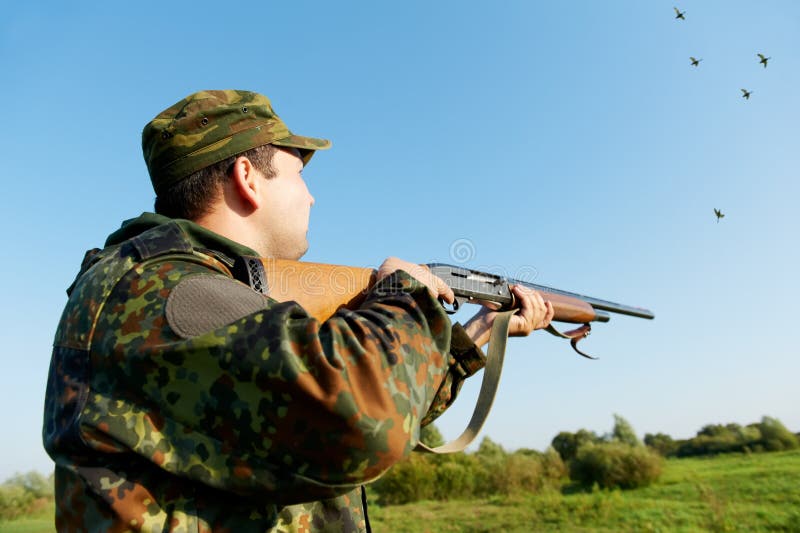 Male hunter in camouflage clothes on the field aiming and shooting with hunting rifle to gamebird during a hunt. Male hunter in camouflage clothes on the field aiming and shooting with hunting rifle to gamebird during a hunt