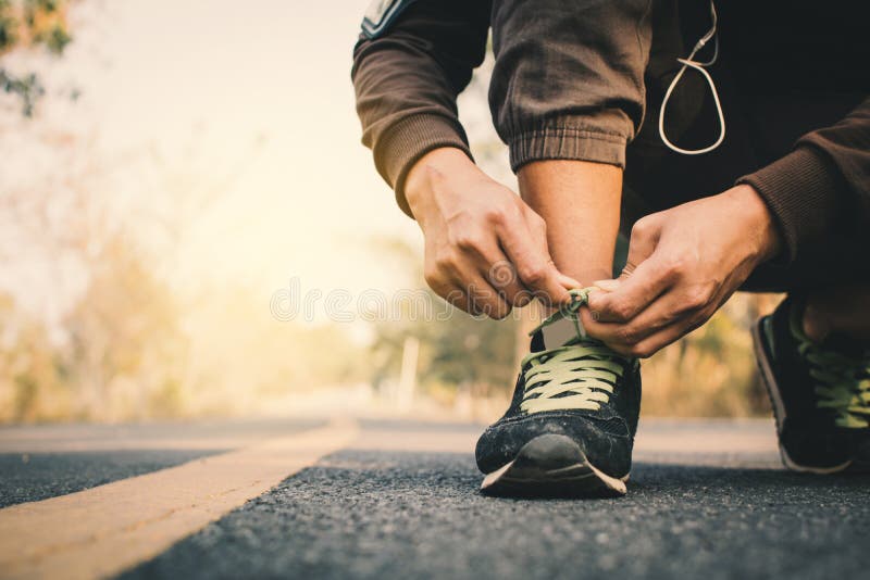 栓鞋带的人的特写镜头手在跑在健康的路期间