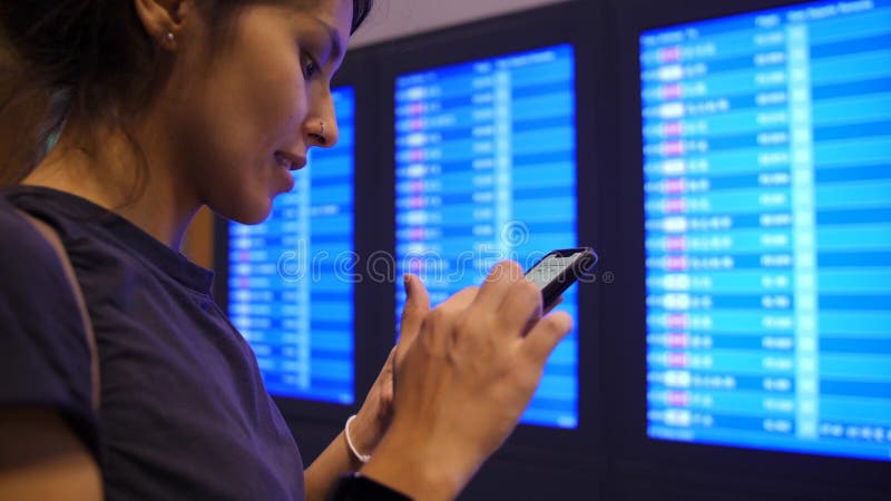 检查她的飞行时间的年轻混合的族种旅游女孩使用手机在离开委员会附近在机场 慢动作的4K 曼谷， 股票录像