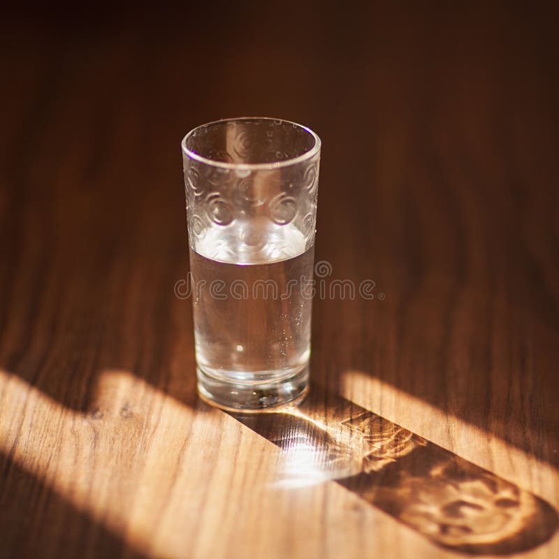 棕色木质背景中的一杯水. 玻璃阴影的刺眼光. 杯子里的纯水. 简单视觉概念. 库存图片