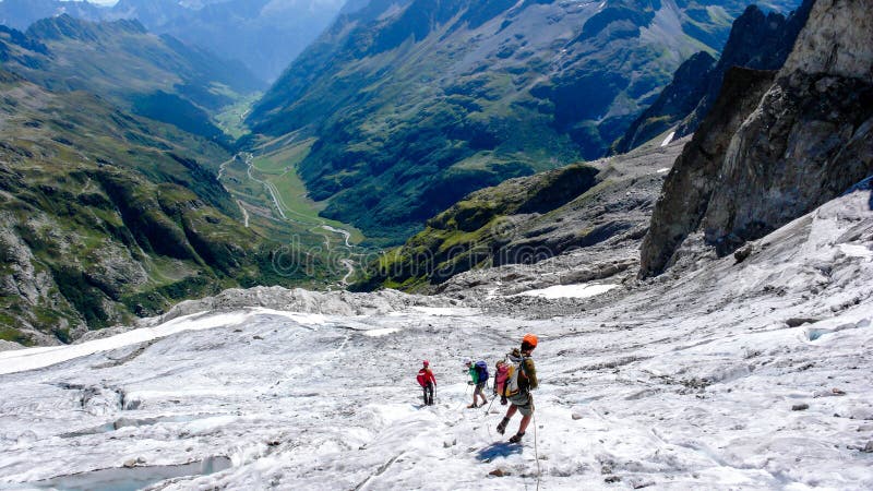 横渡在他们的途中的小组男性爬山者冰川下来从一个高高山峰顶