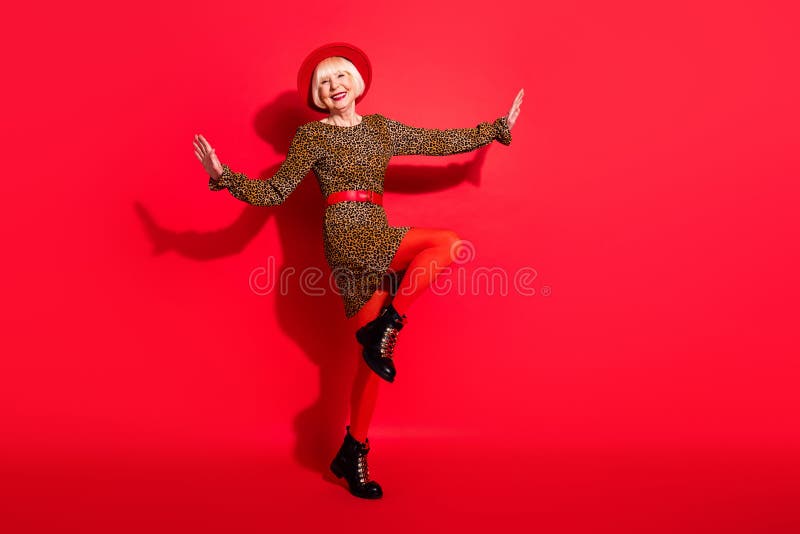 Full body photo of cheerful aged woman happy positive smile enjoy music dance isolated over red color background. Full body photo of cheerful aged woman happy positive smile enjoy music dance isolated over red color background.