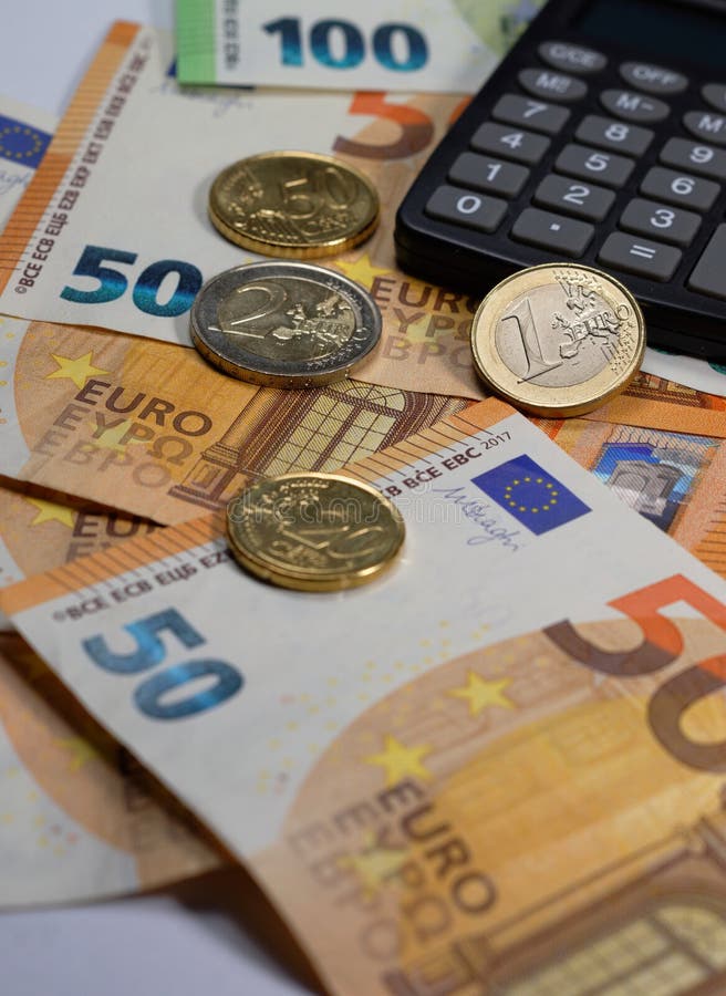Euro 50 and 100 banknotes and coins with partly visible calculator, perspective view with limited in-focus range. Euro 50 and 100 banknotes and coins with partly visible calculator, perspective view with limited in-focus range