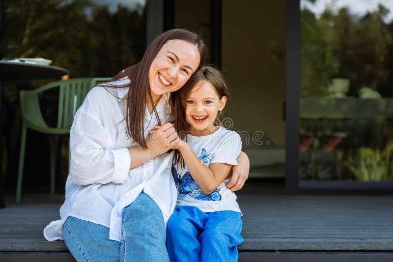 母亲和女儿坐在门廊的台阶上，热情地用手包着对方 免版税库存图片