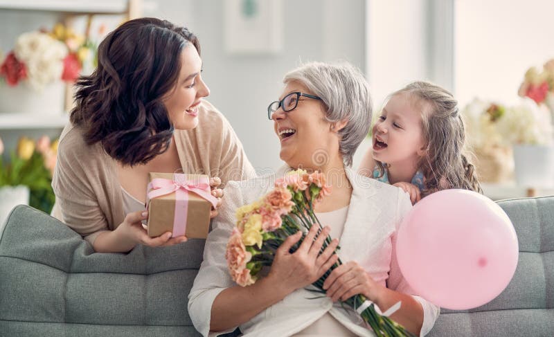 Happy mother`s day! Child daughter is congratulating mom and granny giving them flowers and gift. Grandma, mum and girl smiling and hugging. Family holiday and togetherness. Happy mother`s day! Child daughter is congratulating mom and granny giving them flowers and gift. Grandma, mum and girl smiling and hugging. Family holiday and togetherness