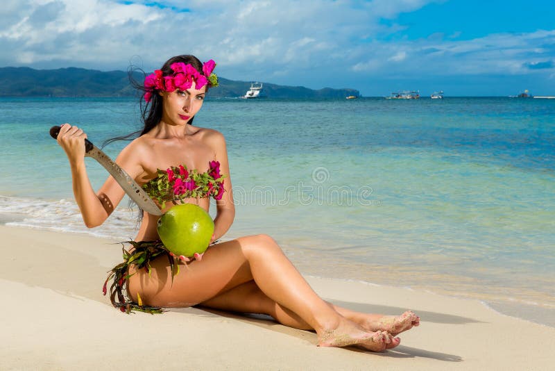 比基尼泳装的年轻美丽的女孩由花制成坐一个热带海滩和椰子与大砍刀 backgroun的蓝色海 库存图片 比基尼泳装的年轻美丽的女孩由花制成坐一个热带海滩和椰子与大砍刀 backgroun的蓝色海 库存图片