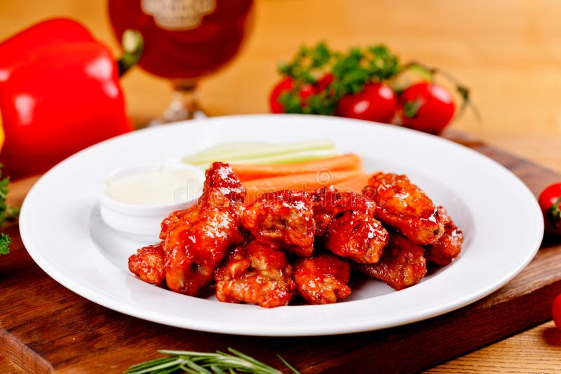 Buffalo chicken wings with blue cheese dip, carrots and celery sticks on white plate. Close up. Buffalo chicken wings with blue cheese dip, carrots and celery sticks on white plate. Close up