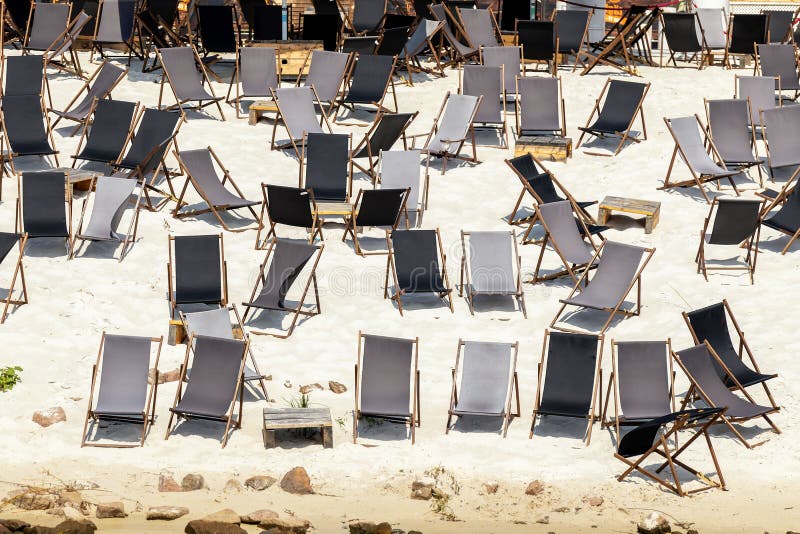 Scenic water view of many empty black wooden deckchair loungers on sand river or sea ocean beach. Rows of deckchair on closed coast due contamination. Lack of people tourist on resort due sanctions. Scenic water view of many empty black wooden deckchair loungers on sand river or sea ocean beach. Rows of deckchair on closed coast due contamination. Lack of people tourist on resort due sanctions.