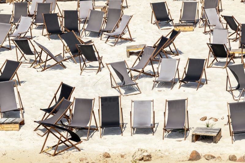 Scenic water view of many empty black wooden deckchair loungers on sand river or sea ocean beach. Rows of deckchair on closed coast due contamination. Lack of people tourist on resort due sanctions. Scenic water view of many empty black wooden deckchair loungers on sand river or sea ocean beach. Rows of deckchair on closed coast due contamination. Lack of people tourist on resort due sanctions.