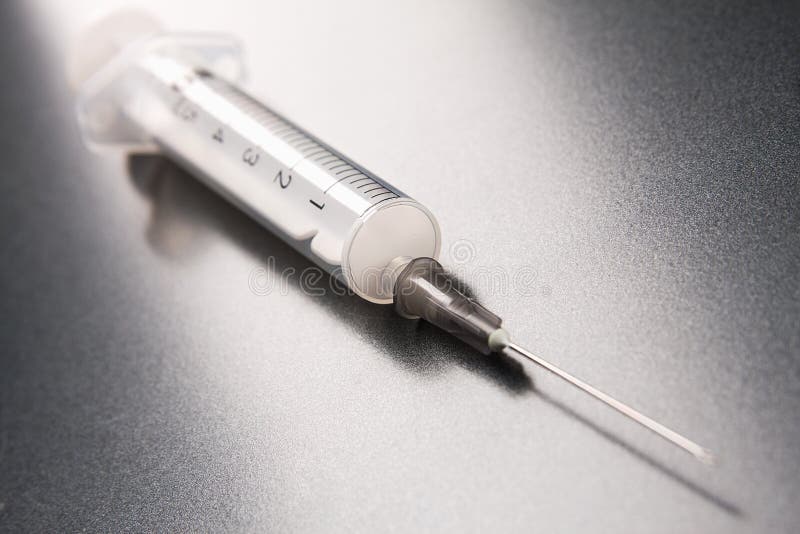 The syringe for an injection lays on a grey background. The syringe for an injection lays on a grey background