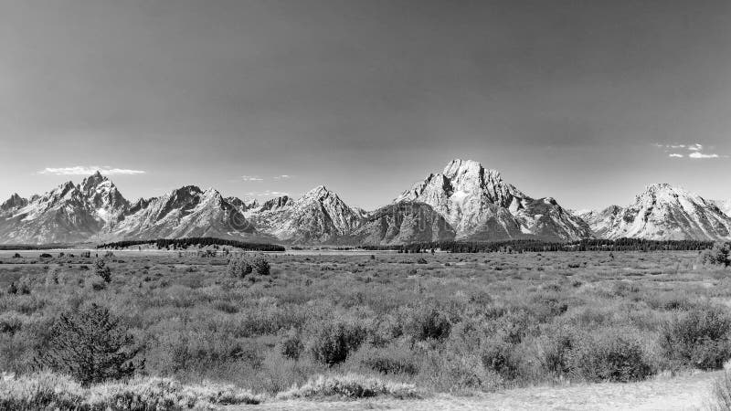 Wide shot of the whole range with Grand Teton on the left, Mount Moran in the middle and Eagle Rest Peak on the right. Broad plain of the potholes with only small shrubs growing because of the high water table. Most grasses and shrubs showing fall colors in early September. The higher peaks show some snow remnants from last winter. Deep haze from smoke from Canadian Forest Fires colors the horizon. Wide shot of the whole range with Grand Teton on the left, Mount Moran in the middle and Eagle Rest Peak on the right. Broad plain of the potholes with only small shrubs growing because of the high water table. Most grasses and shrubs showing fall colors in early September. The higher peaks show some snow remnants from last winter. Deep haze from smoke from Canadian Forest Fires colors the horizon.