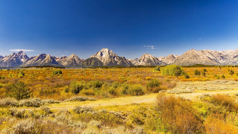 Wide shot of the whole range with Grand Teton on the left, Mount Moran in the middle and Eagle Rest Peak on the right. Broad plain of the potholes with only small shrubs growing because of the high water table. Most grasses and shrubs showing fall colors in early September. The higher peaks show some snow remnants from last winter. Deep haze from smoke from Canadian Forest Fires colors the horizon. Wide shot of the whole range with Grand Teton on the left, Mount Moran in the middle and Eagle Rest Peak on the right. Broad plain of the potholes with only small shrubs growing because of the high water table. Most grasses and shrubs showing fall colors in early September. The higher peaks show some snow remnants from last winter. Deep haze from smoke from Canadian Forest Fires colors the horizon.