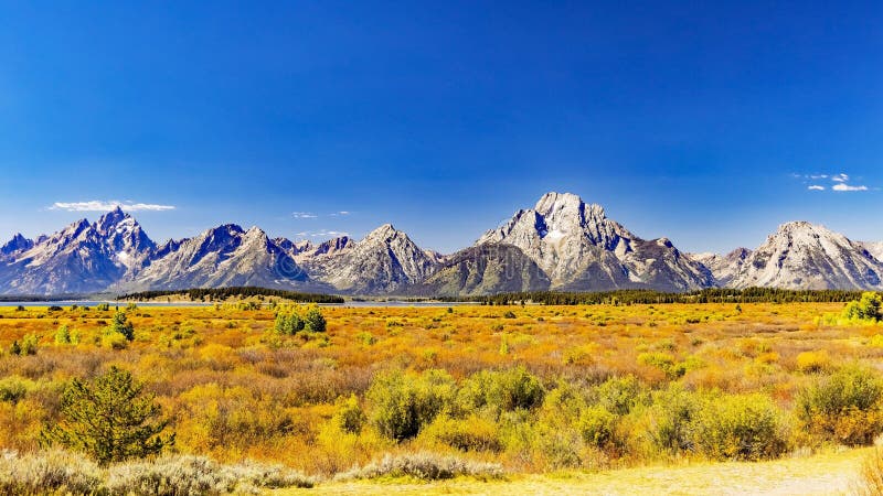 Wide shot of the whole range with Grand Teton on the left, Mount Moran in the middle and Eagle Rest Peak on the right. Broad plain of the potholes with only small shrubs growing because of the high water table. Most grasses and shrubs showing fall colors in early September. The higher peaks show some snow remnants from last winter. Deep haze from smoke from Canadian Forest Fires colors the horizon. Wide shot of the whole range with Grand Teton on the left, Mount Moran in the middle and Eagle Rest Peak on the right. Broad plain of the potholes with only small shrubs growing because of the high water table. Most grasses and shrubs showing fall colors in early September. The higher peaks show some snow remnants from last winter. Deep haze from smoke from Canadian Forest Fires colors the horizon.