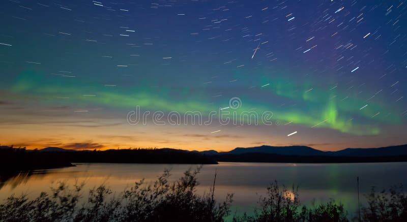 Northern lights Aurora borealis and shooting star meteor at midnight in summer over northern horizon of Lake Laberge Yukon Territory Canada at early dawn. Northern lights Aurora borealis and shooting star meteor at midnight in summer over northern horizon of Lake Laberge Yukon Territory Canada at early dawn