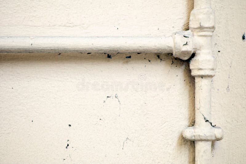 An old intersecting plumber pipe join on a wall background painted over with a cream colour. An old intersecting plumber pipe join on a wall background painted over with a cream colour