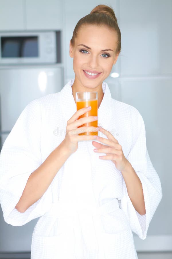Beautiful elegant woman in a white bath robe drinking a large glass of fresh orange juice. Beautiful elegant woman in a white bath robe drinking a large glass of fresh orange juice