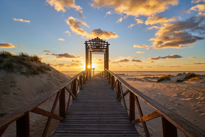 Dramatic sea sunset. The blinding sun hid behind the arch of the wooden bridge. The setting sun sinks into the sea. Dramatic sea sunset. The blinding sun hid behind the arch of the wooden bridge. The setting sun sinks into the sea