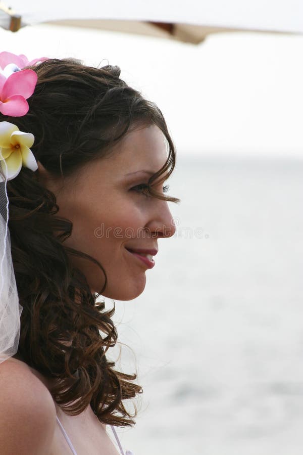 Bride with frangipanis in hair smiling under umbrella on beach. Bride with frangipanis in hair smiling under umbrella on beach