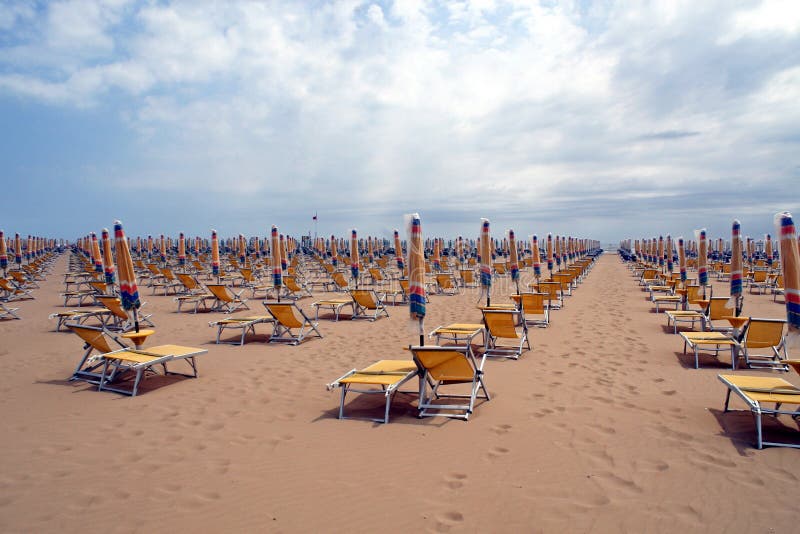 Chairs, beach chairs and umbrellas closed in a line along the sandy shore in a day without sunshine. Chairs, beach chairs and umbrellas closed in a line along the sandy shore in a day without sunshine