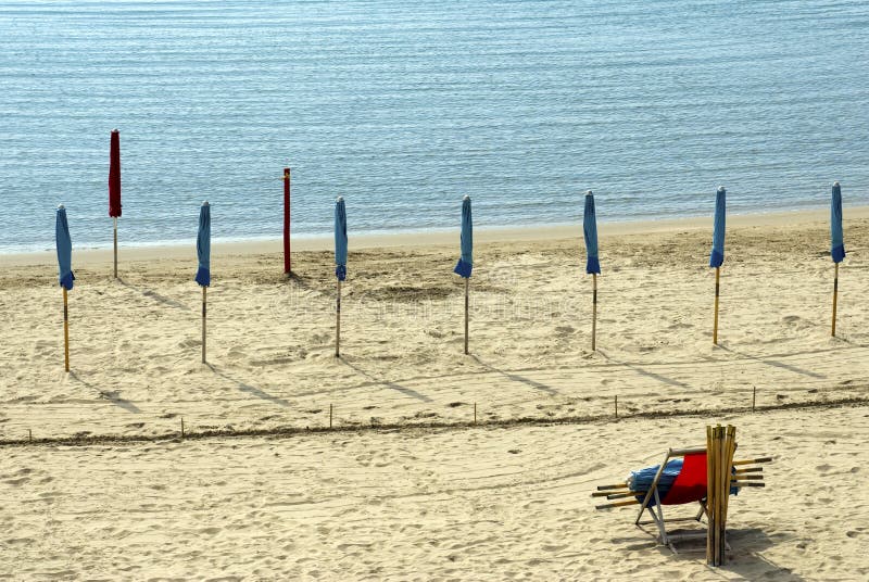 Lines of closed beach-umbrellas along the beach - on a italian beach - Liguria. Lines of closed beach-umbrellas along the beach - on a italian beach - Liguria