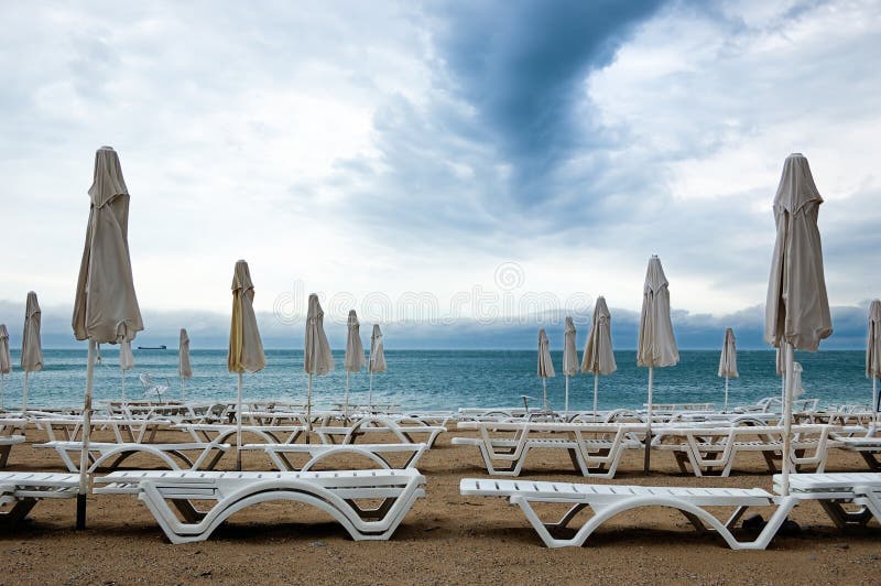 Dead season. Rows of closed umbrellas and deckchairs on the empty beach before a storm. Dead season. Rows of closed umbrellas and deckchairs on the empty beach before a storm.