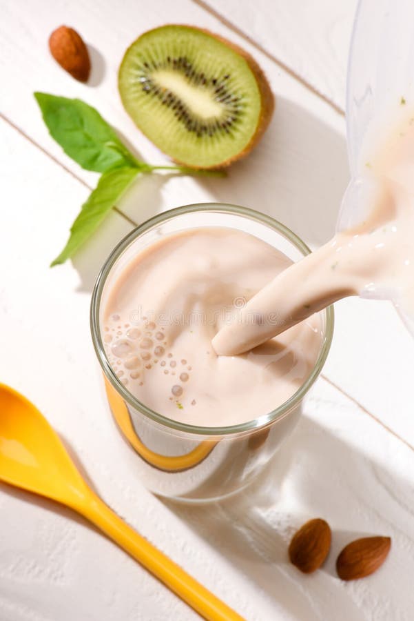 high angle view of protein drink pouring into glass on white wooden table with half of kiwi. high angle view of protein drink pouring into glass on white wooden table with half of kiwi