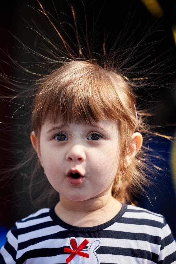 Portrait of a girl with electrified hair on a dark background. Cute small kid girl. Closeup portrait. Electricity power concept. Portrait of a girl with electrified hair on a dark background. Cute small kid girl. Closeup portrait. Electricity power concept