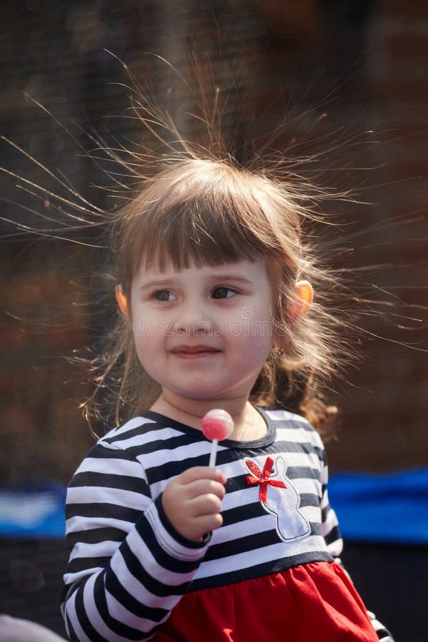 Portrait of a girl with electrified hair on a dark background. Little girl holding a chupa chups with a stick. Electricity power concept. Portrait of a girl with electrified hair on a dark background. Little girl holding a chupa chups with a stick. Electricity power concept