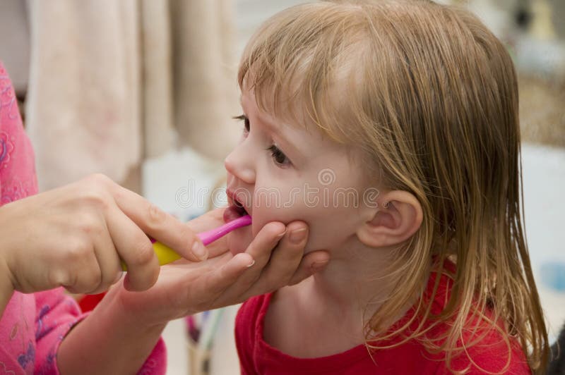 A mother brushes her daughter's teeth. A mother brushes her daughter's teeth