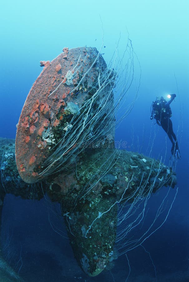 Underwater shoot of female scuba diver swimming near propeller of sunken battleship. Underwater shoot of female scuba diver swimming near propeller of sunken battleship