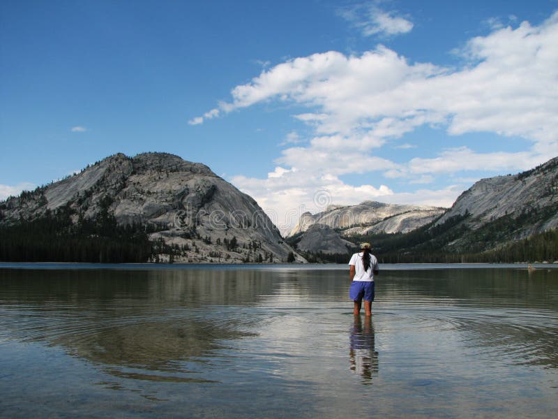 A woman wades in Tenaya Lake in Yosemite National Park with reflection. A woman wades in Tenaya Lake in Yosemite National Park with reflection