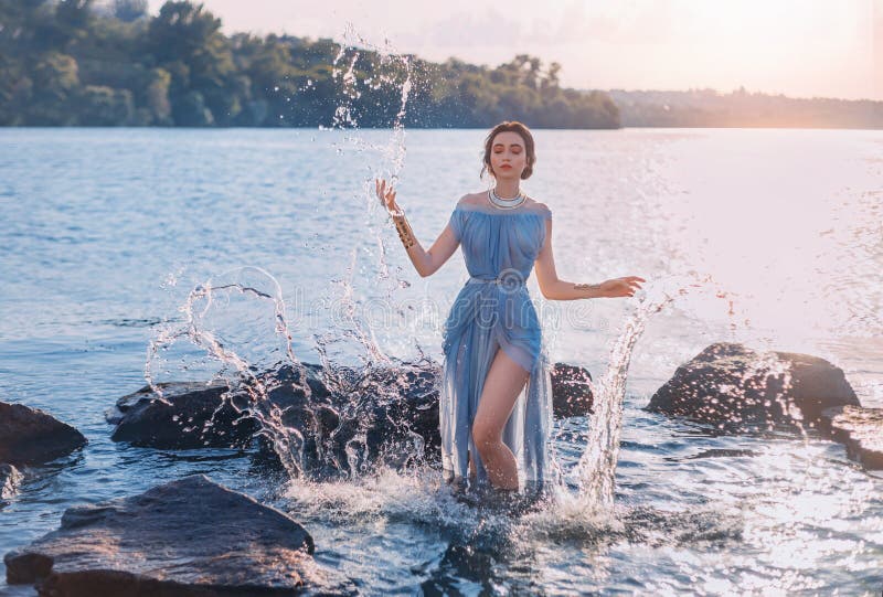 Greek mythical fairytale fantasy woman goddess nymph emerges from lake. Splashes of water. Vintage blue long sexy wet dress. summer nature forest, water surface of river coastal stones. Girl mermaid. Greek mythical fairytale fantasy woman goddess nymph emerges from lake. Splashes of water. Vintage blue long sexy wet dress. summer nature forest, water surface of river coastal stones. Girl mermaid.