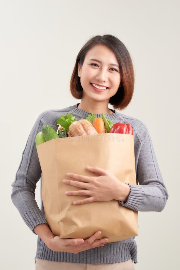 漂亮的微笑亚洲女子拿着装满蔬菜和食品的纸购物袋,工作室被孤立在白色上 库存图片 漂亮的微笑亚洲女子拿着装满蔬菜和食品的纸购物袋,工作室被孤立在白色上 库存图片
