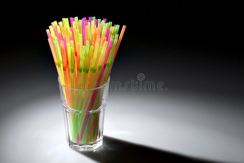 Multicolor flexible straws in the glass in spot of light isolated on black background. Multicolor flexible straws in the glass in spot of light isolated on black background