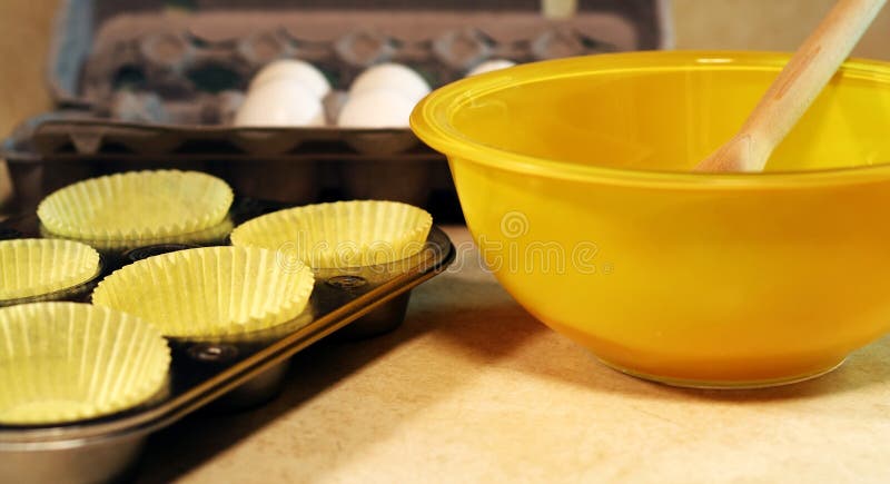 Yellow bowl, muffin tins, eggs; warm lighting. Yellow bowl, muffin tins, eggs; warm lighting