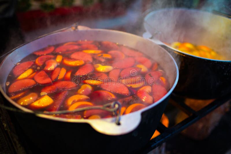 Hot gluhwein or mulled wine in a cauldron at fair, local treat, warm and spicy. A hot wholesome traditional citrus drink on fair. Vitamins in the winter festival. Black pot to cook the mulled wine in the country festival in europe.Christmas market. Hot gluhwein or mulled wine in a cauldron at fair, local treat, warm and spicy. A hot wholesome traditional citrus drink on fair. Vitamins in the winter festival. Black pot to cook the mulled wine in the country festival in europe.Christmas market.