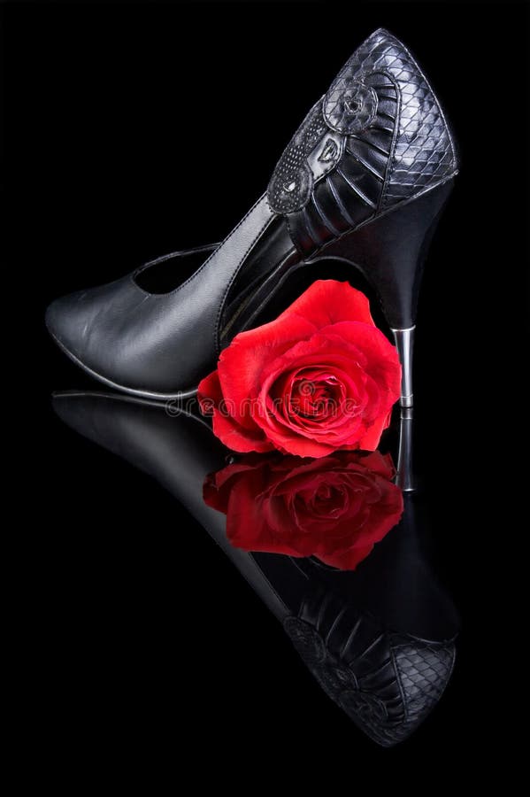 black shoe with high heels, and one red rose on a reflective surface. black shoe with high heels, and one red rose on a reflective surface