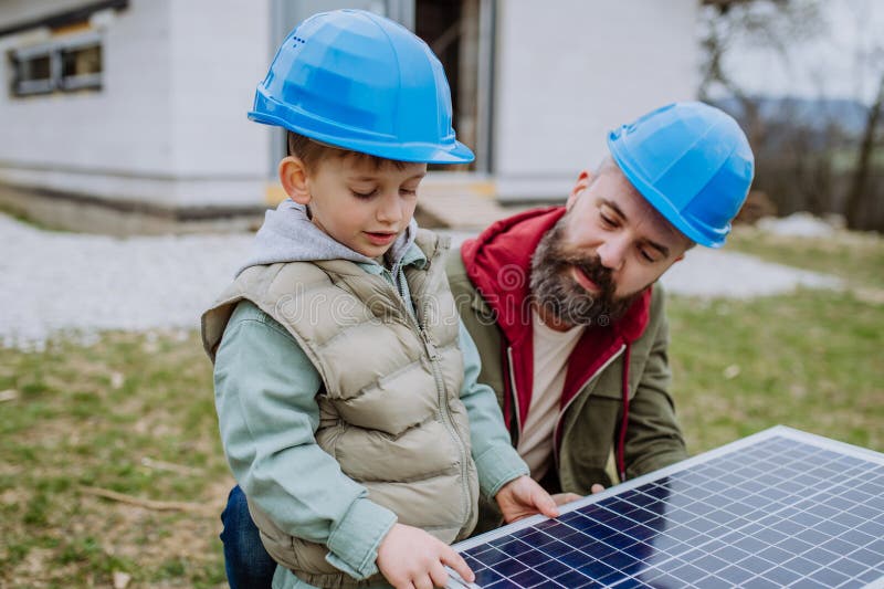 父亲和他小儿子在新未完工房屋前拿着太阳能板的特写.