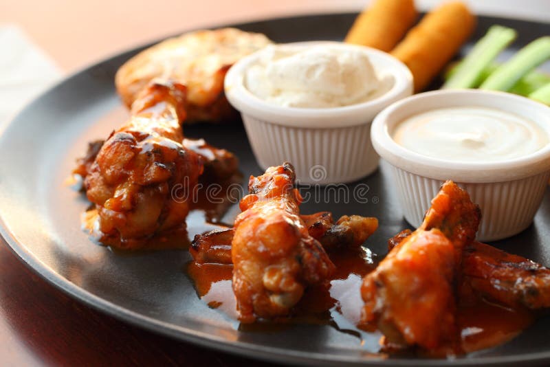 Buffalo wings, sauce, celery, carrots on a black plate. Bokeh effect. Buffalo wings, sauce, celery, carrots on a black plate. Bokeh effect.