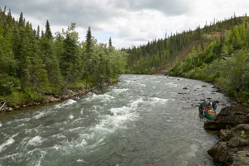 Two men beach their canoe beside turbulent rapids on a wild, remote Alaskan river. Two men beach their canoe beside turbulent rapids on a wild, remote Alaskan river.