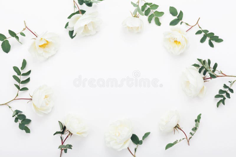 Frame of rose flowers and green leaves on white table top view. Beautiful wedding pattern in flat lay style. Frame of rose flowers and green leaves on white table top view. Beautiful wedding pattern in flat lay style.