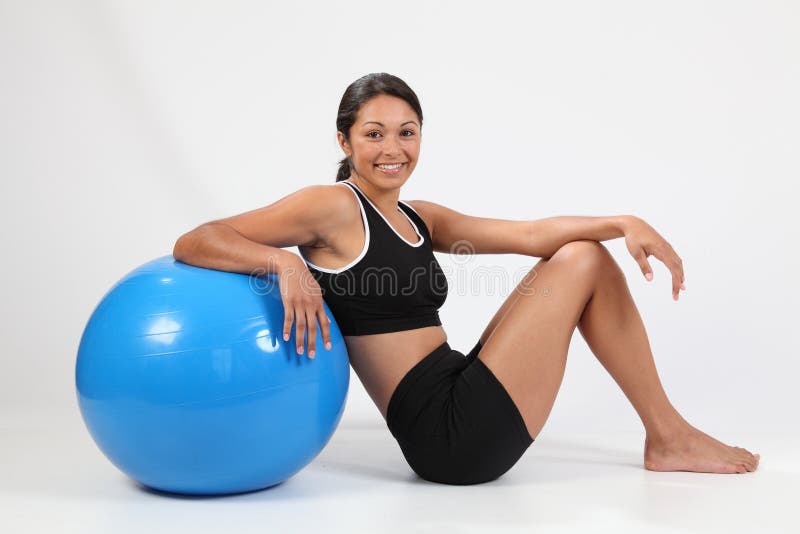 Fit young woman in black sports outfit sitting on floor posing with blue exercise ball and big smile to camera. Studio shot - Canon 5D MKII. Fit young woman in black sports outfit sitting on floor posing with blue exercise ball and big smile to camera. Studio shot - Canon 5D MKII